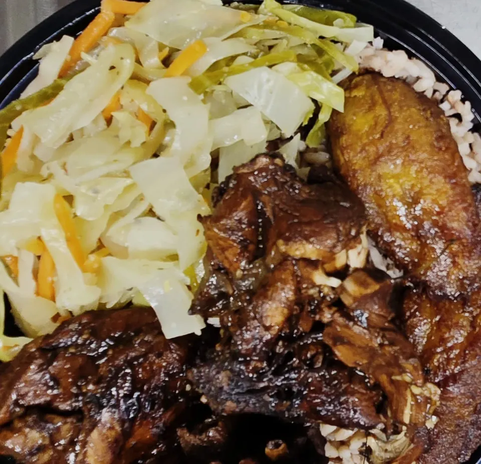Jerk chicken served with rice, steamed cabbage, and fried plantain